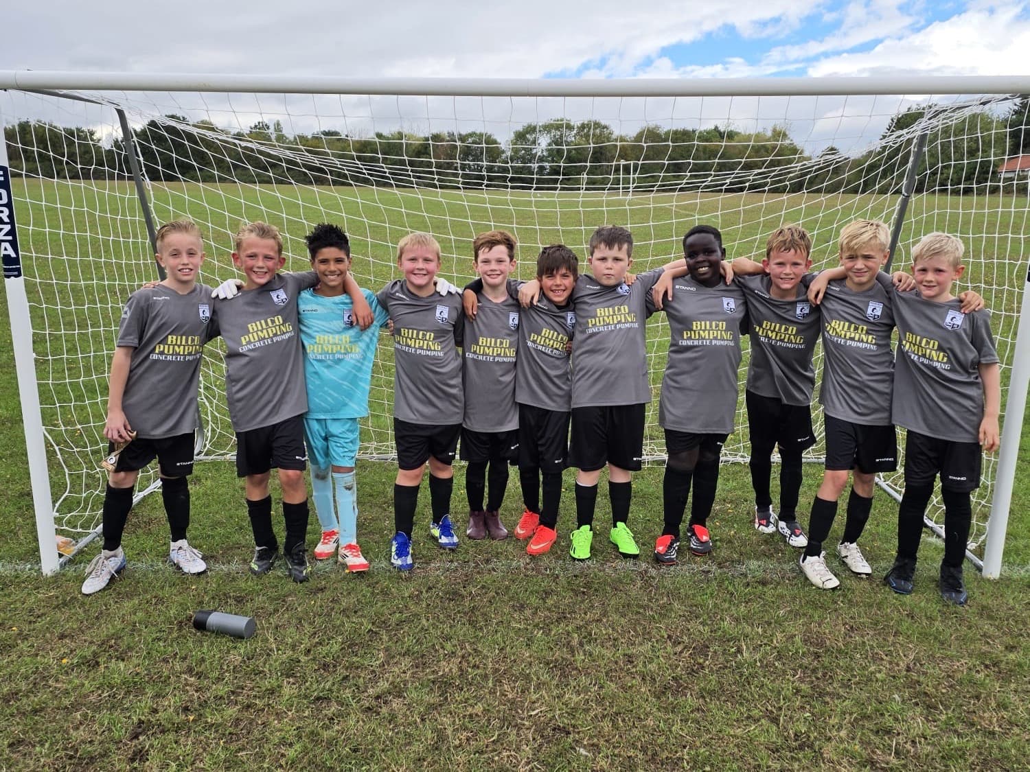 The Wickford Wolves Under 10s team standing together in front of a football goal, wearing grey kits with the Bilco Pumping logo on the front